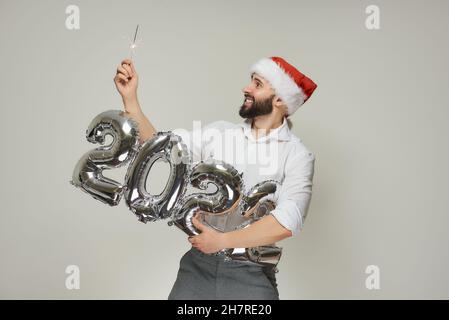 Ein lächelnder Mann in einem roten Samthut hält mit einer Hand silberne Luftballons in der Form von 2022 und mit der anderen Hand einen Funker. Ein Typ mit einem Stockfoto