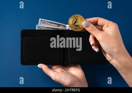 Goldbitcoin und 100-Dollar-Scheine in einer Ledertasche, die von einem Mädchen gehalten wird. Bitcoin mit Dollar in der Brieftasche. Bergmann mit Dollar und Goldbitcoins. Bus Stockfoto