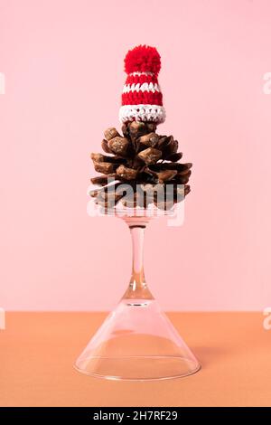 Invertiertes martini-Glas mit Pinecone (Pinus Pinea) und Santa-Hut auf rosa Hintergrund. Vertikales Foto Stockfoto