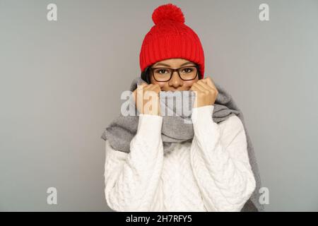 Lustige junge afrikanische Frau im Pullover, gestrickter Wollhut versteckt Lächeln unter warmen Schal bedeckendes Gesicht Stockfoto