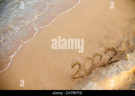 2022 Zahlen sind auf Sand am Strand geschrieben. Das neue Jahr 2021 steht vor dem Konzept. Hintergrund für das Neujahrsbanner oder die Werbung Stockfoto