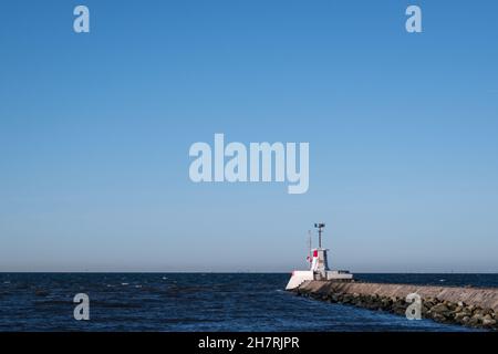 Ein weißer und roter Leuchtturm auf einem Steinpier und Wellenbrecher am Hafeneingang in Lomma Schweden Stockfoto