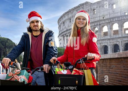 Schöne Weihnachtseinkäufe in Rom mit gemieteten Fahrrädern. Ein junges Paar, das sich von ihren Geschäften in der Nähe des Kolosseums ausruhen kann. Stockfoto