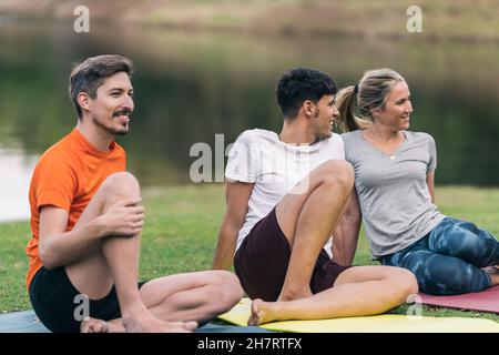 Entspannte Gruppe von Freunden, die auf einer Yogamatte in einem Park sitzen Stockfoto