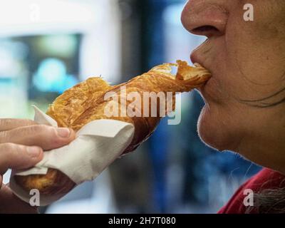 Eine alte hispanische Frau, die in einem Café ein Croissant isst Stockfoto
