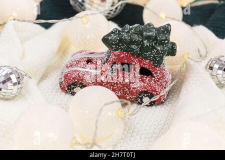 Rotes Auto mit Weihnachtsbaum auf weißem Pullover, LED-Leuchten. Weihnachtsdekoration auf dem Schnee Stockfoto