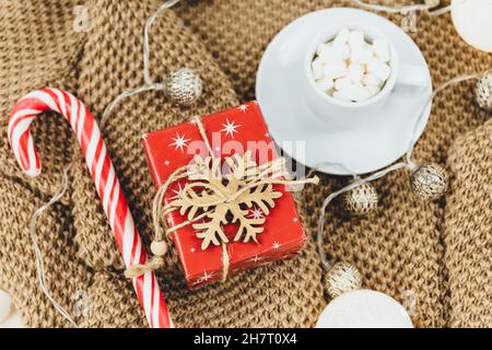 Tasse Kaffee, Geschenkbox und Strickpullover, LED-Leuchten auf beigem Hintergrund. Hygge-Stil, Winterkonzept. Gemütlicher Schreibtisch. Neujahr und Weihnachten Stockfoto