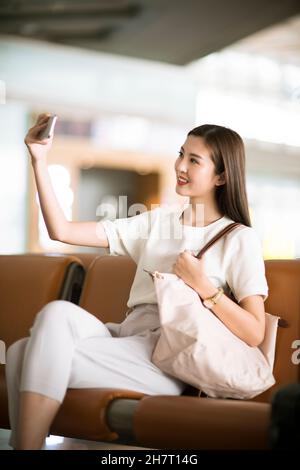 Ein junges Paar, das Selfies auf dem Handy in einer Lounge am Flughafen macht Stockfoto