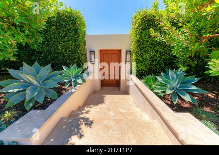 Unten Eingang mit Marmorfliesen und Holztür in La Jolla, Kalifornien. Moderne Residenz mit Rosettenpflanzen und Sträuchern auf beiden Seiten des Do Stockfoto