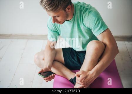 Mann chattet am Telefon nach dem Training zu Hause. Quarantäne-Lebensstil. Gesunder Lebensstil. Stockfoto
