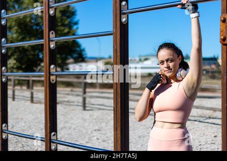 Eine athletische kaukasische Frau mit Kopfhörern in einem Calisthenics-Barpark Stockfoto