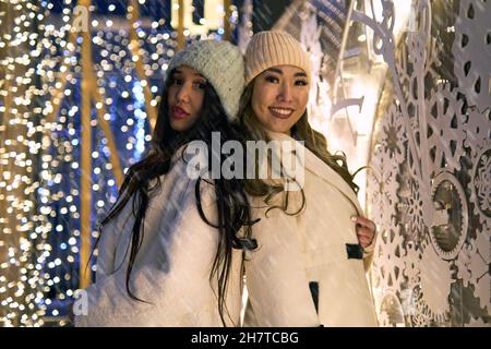 Zwei Freundinnen asiatische Mädchen in weißen Mänteln haben Spaß Umarmung, Neujahr, Glühbirnen Stockfoto