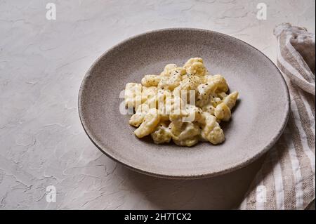 Nahaufnahme hausgemachter Gnocchi, zubereitet mit Kartoffel- und Vollkornmehl-Teig mit Sahnesauce auf grauem Betongrund mit Serviette Stockfoto