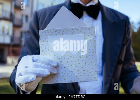 Die Hand eines Mannes in einem weißen Handschuh hält einen offenen Umschlag mit einem Platz für Text Stockfoto