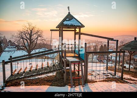 Der Kinderspielplatz ist mit Schnee bedeckt und an einem kalten Wintertag in Österreich leer Stockfoto