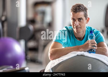 Der Mann, der eine Wasserflasche hält, ruht während eines Trainings im Fitnessstudio. Stockfoto