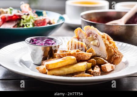 Chicken Cordon Bleu mit Schinken und Käse im Inneren serviert mit gebratenen Kartoffelscheiben und Rotkohlsalat. Stockfoto