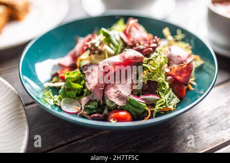 Dünn geschnittenes Roastbeef serviert auf einem knusprigen slad mit Karotten, Kirschtomaten und Radieschen. Stockfoto