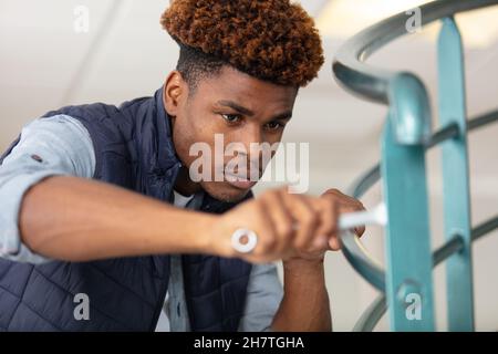 Junger Mann, der Schrauben auf einem Geländer festzieht Stockfoto