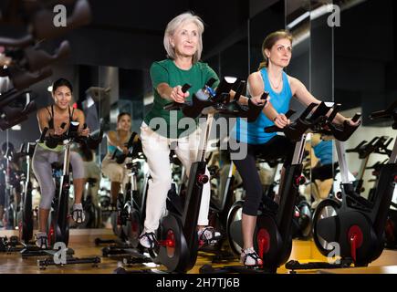 Frauen trainieren auf stationären Fahrrädern im Fitnessstudio Stockfoto