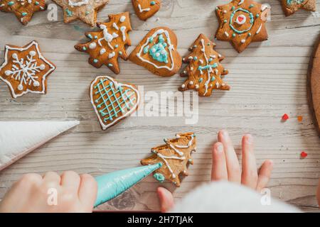 Teilweise verschwommene Hände von Jungen schmücken Lebkuchenkekse mit blauer Glasur in der Küche. Das Kind bereitet Kekse auf einem Holztisch zu. Frohe Weihnachten, Glücklich Stockfoto