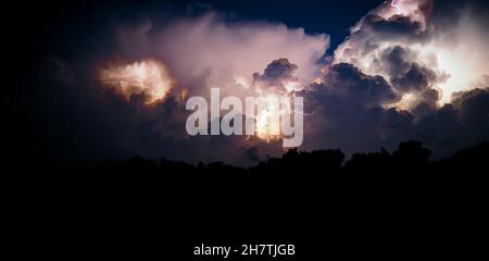 Elektrische Entladungen des Blitzes am Nachthimmel. Gewitterwolken und Blitze blitzen während eines Gewitters in der Nacht auf. Panoramafoto. Stockfoto