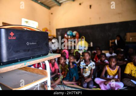 Dakar, Senegal. 22nd. November 2021. Die Schüler sehen Satellitenfernsehen über einen Projektor des chinesischen Medienunternehmens StarTimes im Rahmen eines von China finanzierten Projekts an einer Schule am Stadtrand von Dakar, Senegal, am 22. November 2021. Das Satelliten-TV-Projekt ist eines der Früchte der Resolutionen des Gipfels des Forums über die Zusammenarbeit zwischen China und Afrika 2015 in Johannesburg, Südafrika, bei dem die chinesische Regierung zugesagt hat, in 10.000 afrikanischen Dörfern Satellitenfernsehen bereitzustellen. Kredit: Li Yan/Xinhua/Alamy Live Nachrichten Stockfoto