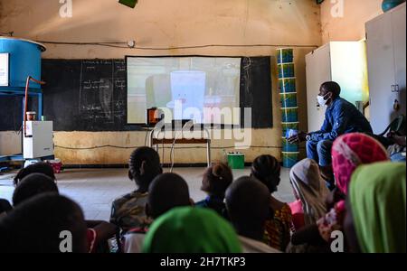 Dakar, Senegal. 22nd. November 2021. Die Schüler sehen Satellitenfernsehen über einen Projektor des chinesischen Medienunternehmens StarTimes im Rahmen eines von China finanzierten Projekts an einer Schule am Stadtrand von Dakar, Senegal, am 22. November 2021. Das Satelliten-TV-Projekt ist eines der Früchte der Resolutionen des Gipfels des Forums über die Zusammenarbeit zwischen China und Afrika 2015 in Johannesburg, Südafrika, bei dem die chinesische Regierung zugesagt hat, in 10.000 afrikanischen Dörfern Satellitenfernsehen bereitzustellen. Kredit: Li Yan/Xinhua/Alamy Live Nachrichten Stockfoto