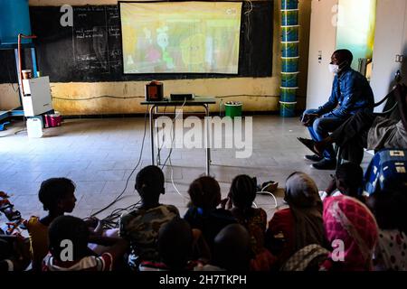 Dakar, Senegal. 22nd. November 2021. Die Schüler sehen Satellitenfernsehen über einen Projektor des chinesischen Medienunternehmens StarTimes im Rahmen eines von China finanzierten Projekts an einer Schule am Stadtrand von Dakar, Senegal, am 22. November 2021. Das Satelliten-TV-Projekt ist eines der Früchte der Resolutionen des Gipfels des Forums über die Zusammenarbeit zwischen China und Afrika 2015 in Johannesburg, Südafrika, bei dem die chinesische Regierung zugesagt hat, in 10.000 afrikanischen Dörfern Satellitenfernsehen bereitzustellen. Kredit: Li Yan/Xinhua/Alamy Live Nachrichten Stockfoto