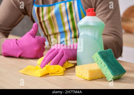 Junger, gutaussehender Mann in der Küche, reinigt mit Waschmitteln, Bürsten, Sprays Stockfoto