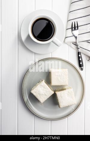 Süßer Kuchen und Kaffeebecher. Leckeres Kokosnussdessert auf dem Teller. Draufsicht. Stockfoto