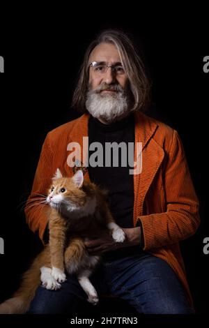 Grauhaariger bärtiger Intellektueller im reifen Alter, der mit einer Ingwer-angepassten Katze posiert Stockfoto