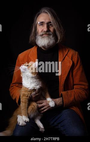 Grauhaariger bärtiger Intellektueller im reifen Alter, der mit einer Ingwer-angepassten Katze posiert Stockfoto