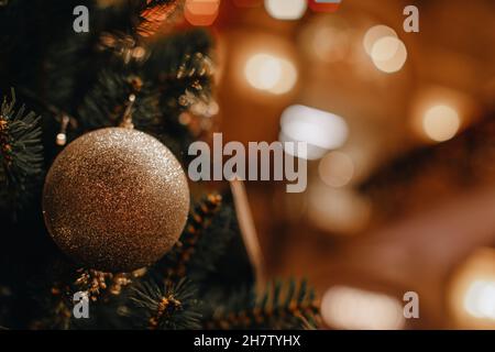 Goldene Weihnachtskugel, die auf dem Weihnachtsbaum hängt. DefokussierteGirlande-Lichter, Bokeh-Magieeffekt. Festlicher Hintergrund Stockfoto