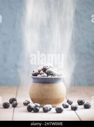 Eine Tasse aus Steinzeug, gefüllt mit Heidelbeeren auf einer keramischen Oberfläche. Staubpulver an die Beeren gesiebt Stockfoto