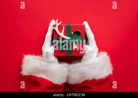 Der Weihnachtsmann hält eine Geschenkschachtel mit einem roten Hintergrund Stockfoto