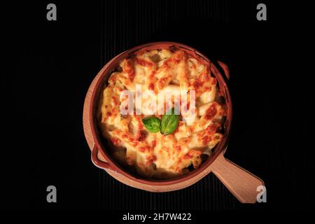 Penne Pasta in rustikalen Tellern auf einer Holzplatte isoliert auf schwarzem Hintergrund. Stockfoto