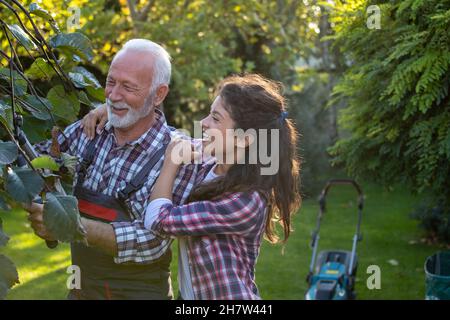 Der ältere Mann Schnitt Zweige von Bäumen, während die hübsche Tochter ihn im Garten umarmte Stockfoto