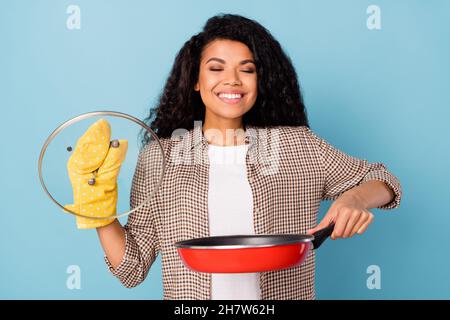 Portrait von attraktiven trendy verträumt fröhliche Mädchen halten Pfanne riechend frisch schmackhafte Mahlzeit isoliert über hellblauen Hintergrund Stockfoto