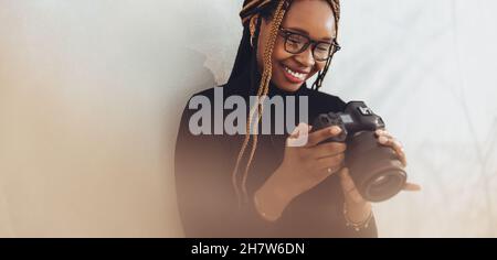 Machen Sie sich bereit, ein paar Bilder aufzunehmen. Glückliche Fotografin lächelt fröhlich, während sie ihre dslr-Kamera in ihrem Heimbüro aufsetzt. Kreative fe Stockfoto