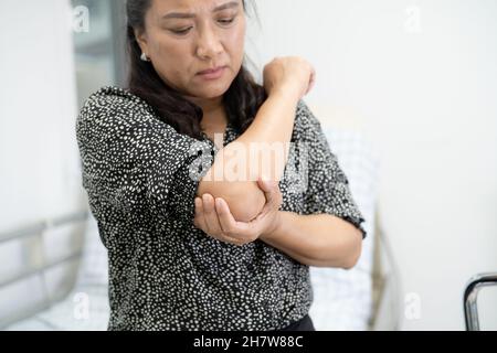 Asiatische Frau mittleren Alters Frau Patientin berühren und fühlen Schmerzen ihren Ellbogen und Arm, gesunde medizinische Konzept. Stockfoto
