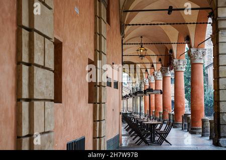 Restaurant ohne Kunden in Bologna während der Corona-Pandemie. Leere Tische und Stühle auf dem Bürgersteig in der Arkade davor. Stockfoto