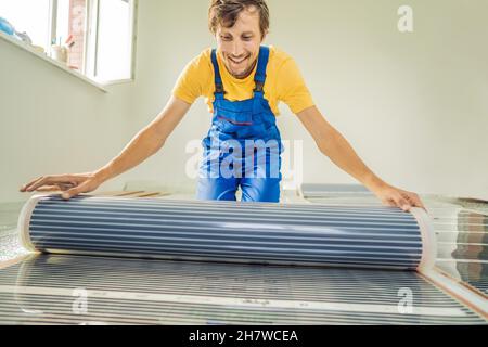 Master installiert einen warmen Fußboden im Raum. Installation der Fußbodenheizung Stockfoto