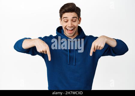 Hey, schau mal. Lächelnder aufgeregt Kerl zeigt die Finger nach unten, zeigt Werbung, demonstriert Promo-Angebot, weißer Hintergrund Stockfoto