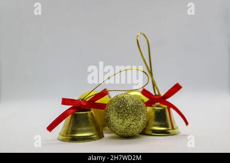 Goldfarbene Glocken und Kugeln, Glocken mit roten Schleifen, Weihnachtsdekoration auf weißem Hintergrund, Neujahrsdekoration, Weihnachtskarte, Stockfoto