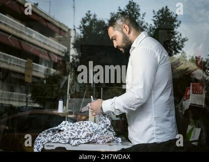 Junger Mann aus dem Nahen Osten, der in seiner Schneiderei arbeitet. Konzept für kleine Unternehmen oder Selbstständige Stockfoto