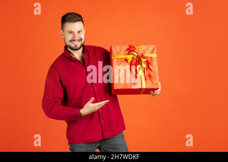 Beschnittenes Porträt eines Mannes im Hemd mit Geschenkbox, der fröhlich auf rotem Hintergrund posiert Stockfoto