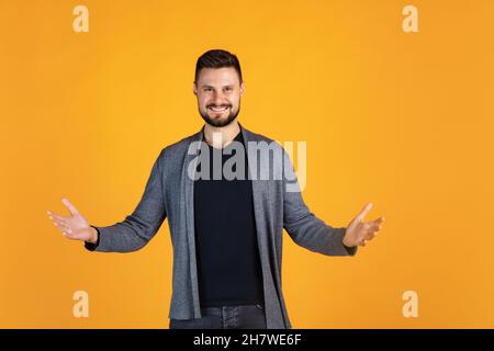 Verkürztes Porträt eines glücklichen und aufgeregten Mannes in grauer Strickjacke, der fröhlich isoliert auf gelbem Hintergrund posiert Stockfoto