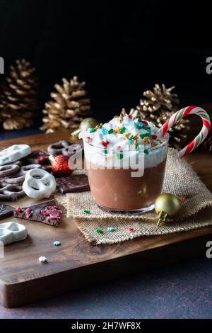 Heiße Schokolade mit Peitschencreme und Weihnachtsstreuseln vor dunklem Hintergrund. Stockfoto