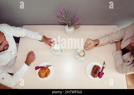 Frühstück. Mann und Frau frühstücken im Café. Kaffee und Brötchen. Gebäck auf Holztisch. Arbeiterfrühstück. Im Café. Stockfoto